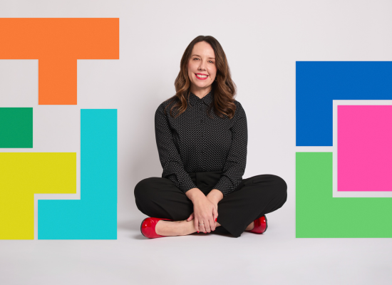 Woman in black outfit and red shoes, seated cross-legged among colorful geometric shapes, showcasing event storytelling experience.